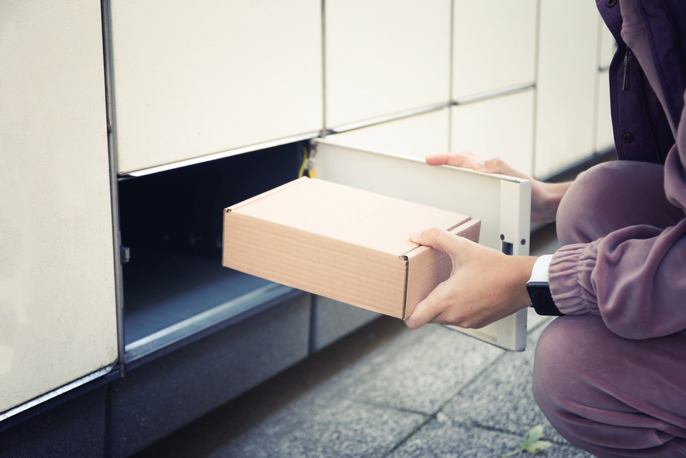 Kundin gibt ein Paket im Hermes-Paketshop ab und Paketstation im Hintergrund